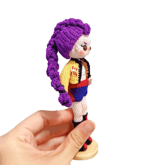 Hand holding a small crochet doll with purple hair on a white background