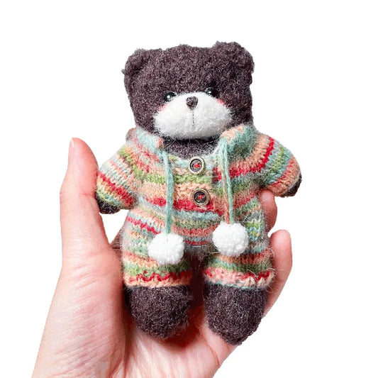 Small teddy bear wearing a colorful striped sweater held in a hand against a white background