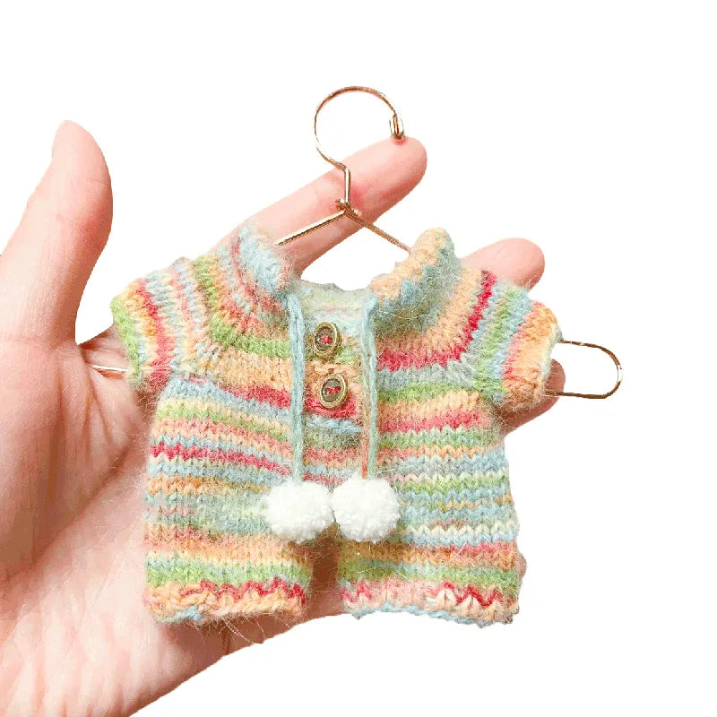 Small striped knitted cardigan with pom-poms held in a hand against a white background