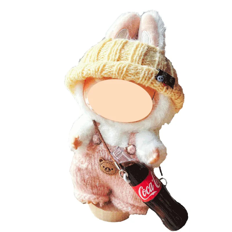 Plush toy resembling a rabbit wearing a yellow hat with a Coca-Cola bottle charm on a white background