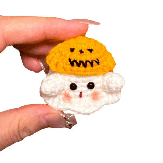 Hand holding a small crocheted character with a yellow pumpkin hat and white face.