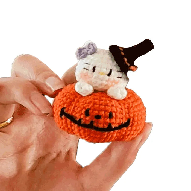 Hand holding a small crocheted Halloween-themed plush toy with a pumpkin base and cat-like figure.