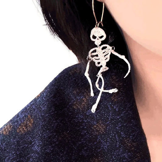 Skeleton-shaped earring worn by a person with a dark background