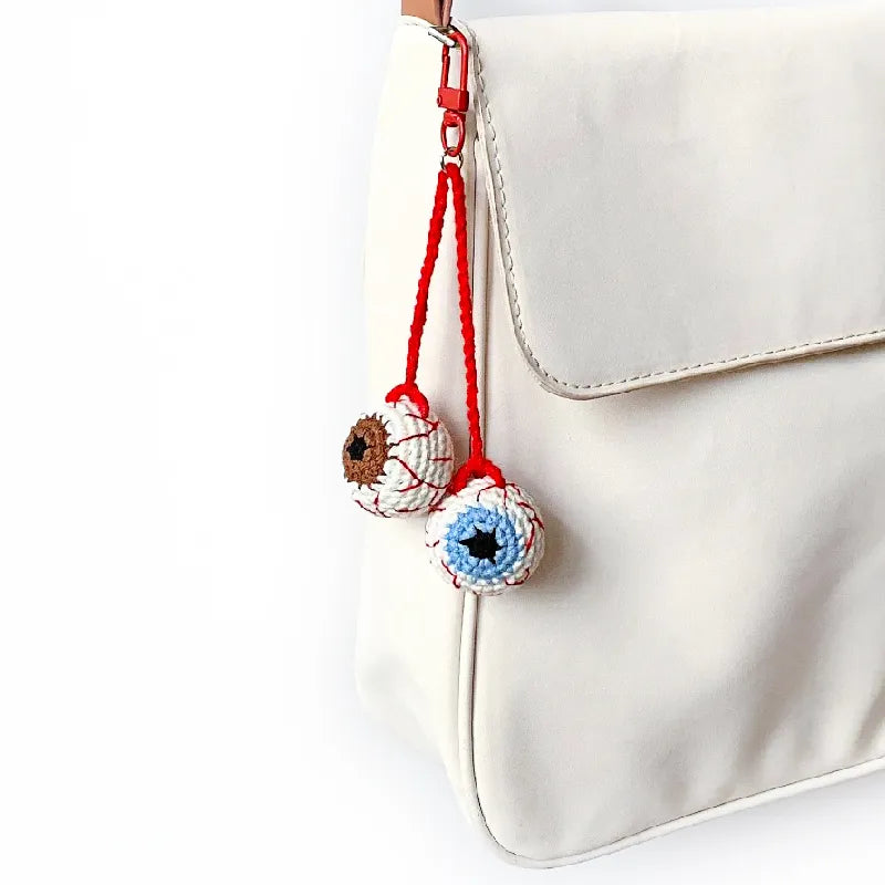 Decorative keychain with eye design hanging from a white bag.