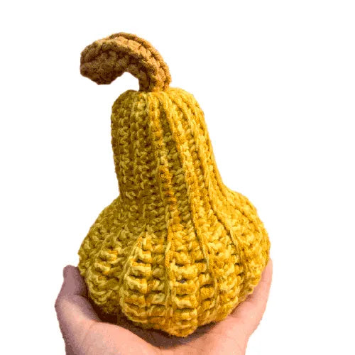 Hand holding a knitted yellow gourd against a white background