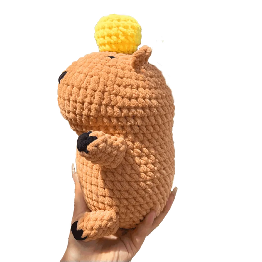 Hand holding a handmade amigurumi capybara plushie tutorial with a yellow pom pom on top