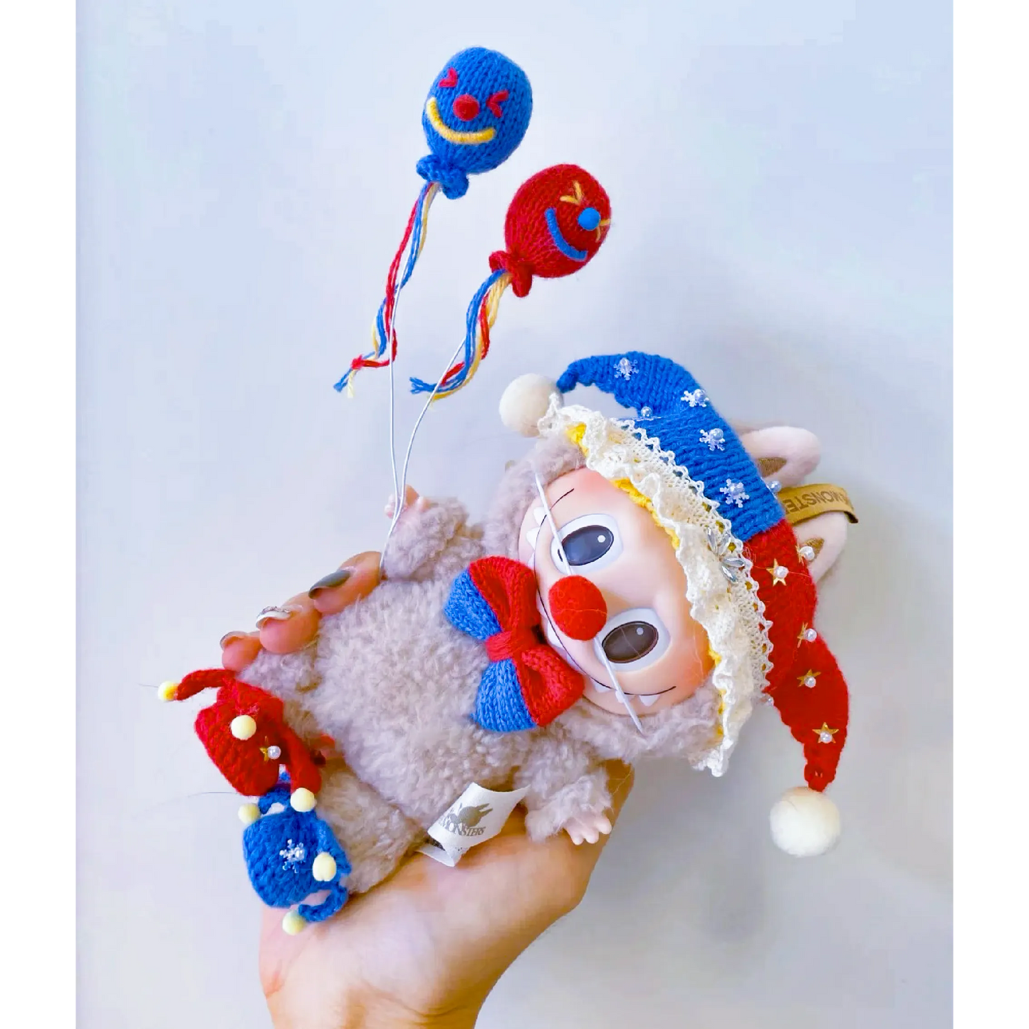 Hand holding a crochet clown doll with red and blue hat and blue red balloons Circus Clown Crochet Pattern