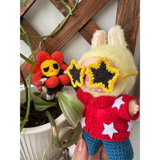 Collectible doll crochet design with star-shaped yellow sunglasses and red star sweater holding a crocheted flower figure