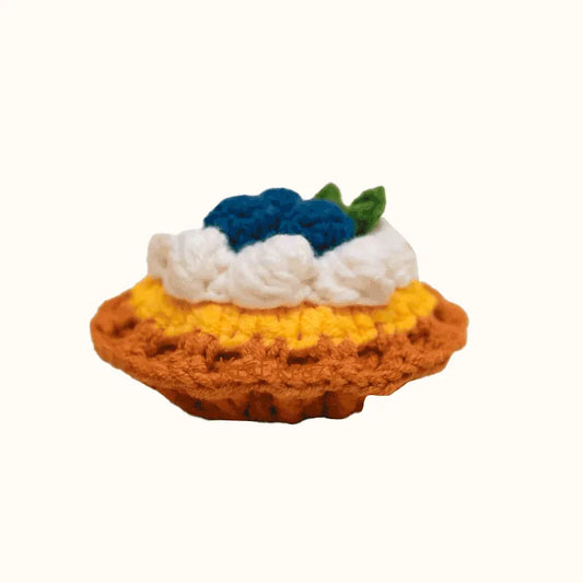 Handmade crochet blueberry tart pattern with brown crust, yellow filling, white cream, and blue berry topping