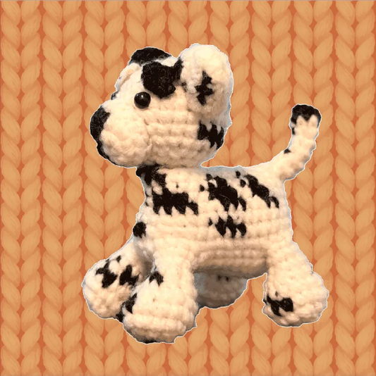 Handmade crochet Dalmatian dog pattern with black spots on white yarn against knitted background