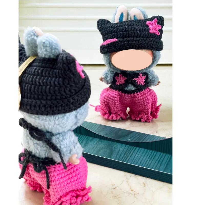 Handmade crochet doll outfit with black hat and pink pants displayed on doll in front of mirror