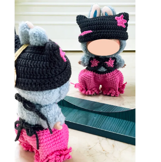 Handmade crochet doll outfit with black hat and pink pants displayed on doll in front of mirror