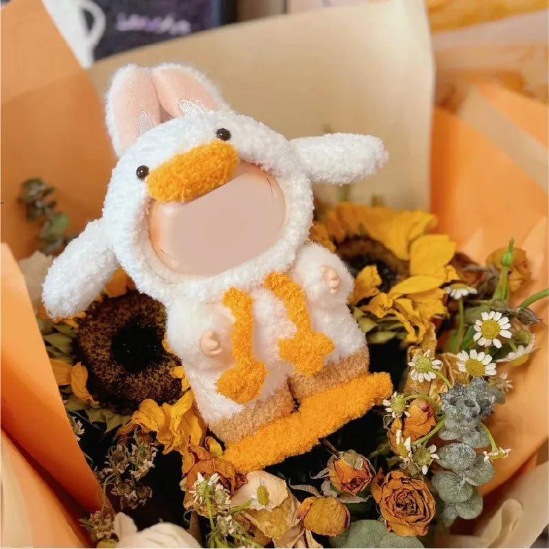 Crochet duck doll pattern featuring a cute plush duck with orange beak and feet surrounded by dried flowers