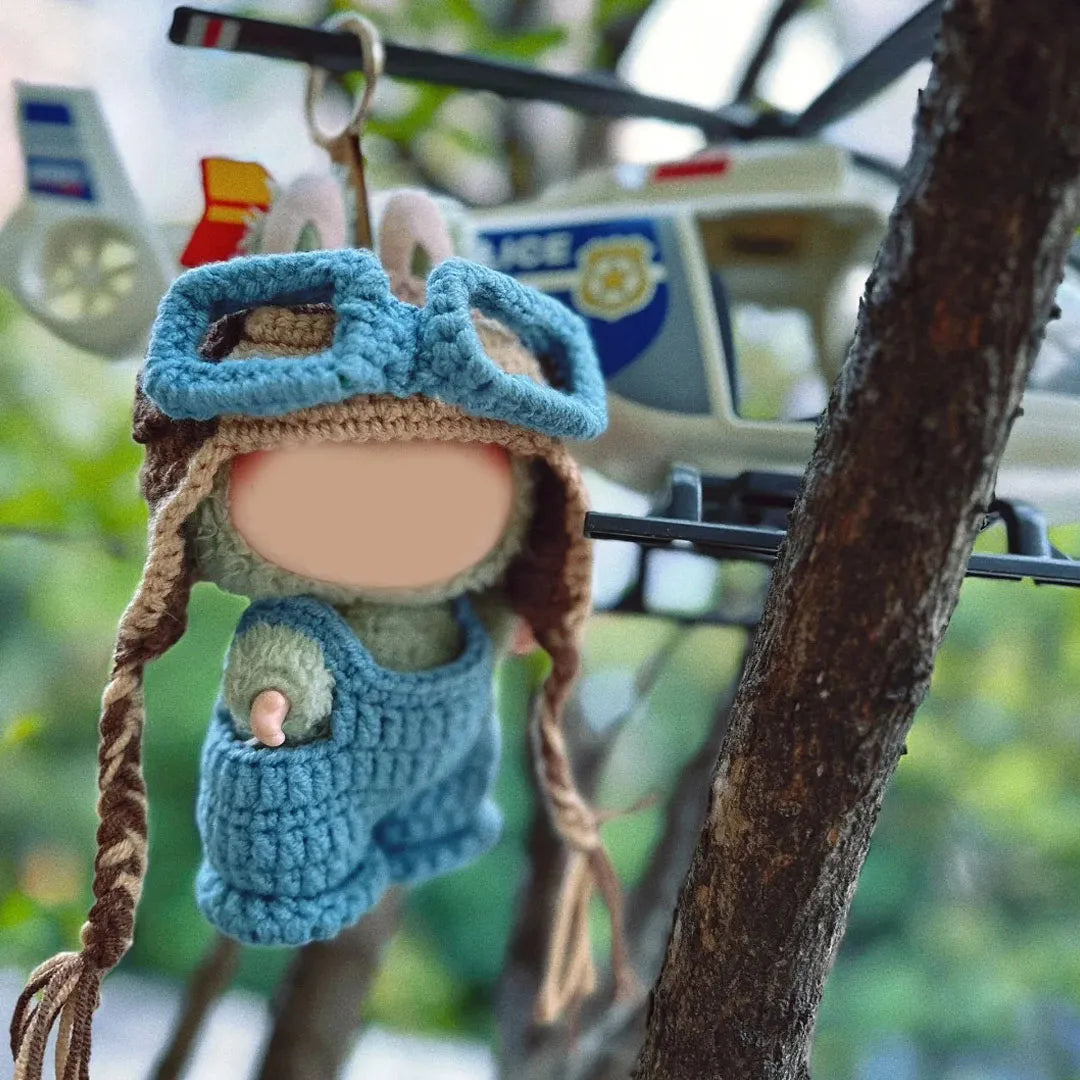 Handmade crochet doll wearing blue crochet pilot hat pattern and overalls hanging near toy helicopter