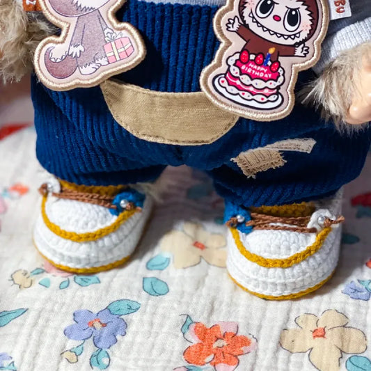 White and yellow crochet shoes for 38cm plush dolls worn by a doll dressed in blue pants