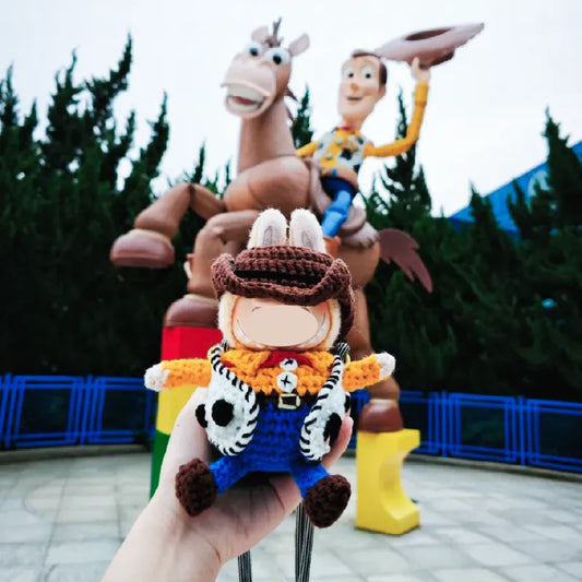 Hand holding a crochet woody doll bag pattern with large Woody and horse statue in background