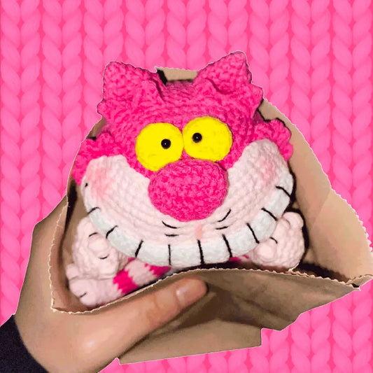 Pink crocheted Cheshire Cat toy with yellow eyes and big smile using free crochet cheshire cat pattern