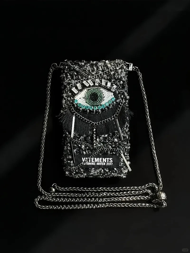 FREE|cyberpunk crochet phone bag pattern featuring a black bag with a detailed eye design and metal chain strap