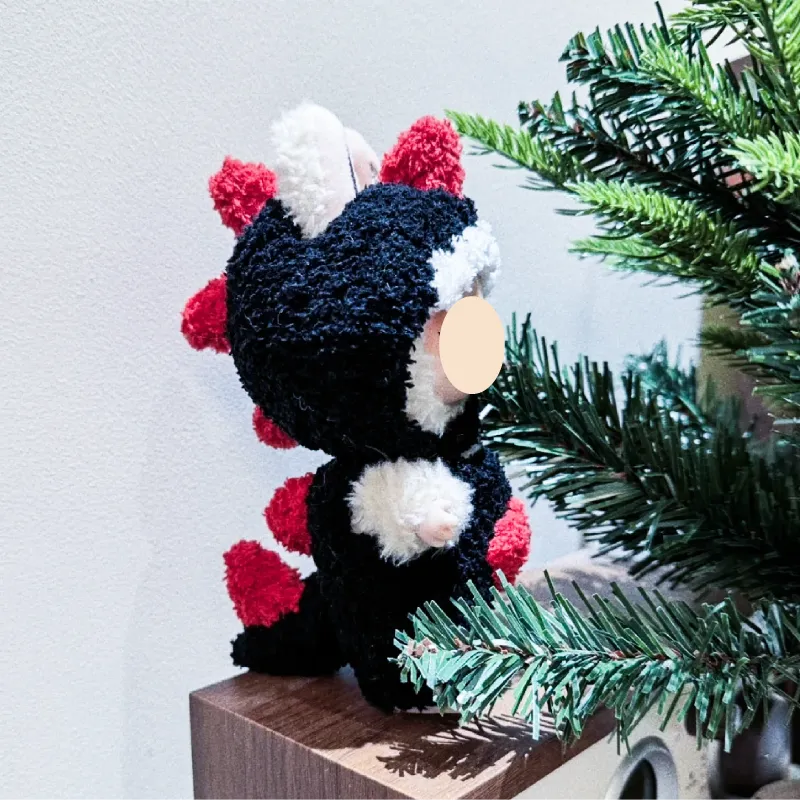 Handmade black and red crochet dinosaur toy displayed next to green pine branches free dinosaur crochet pattern