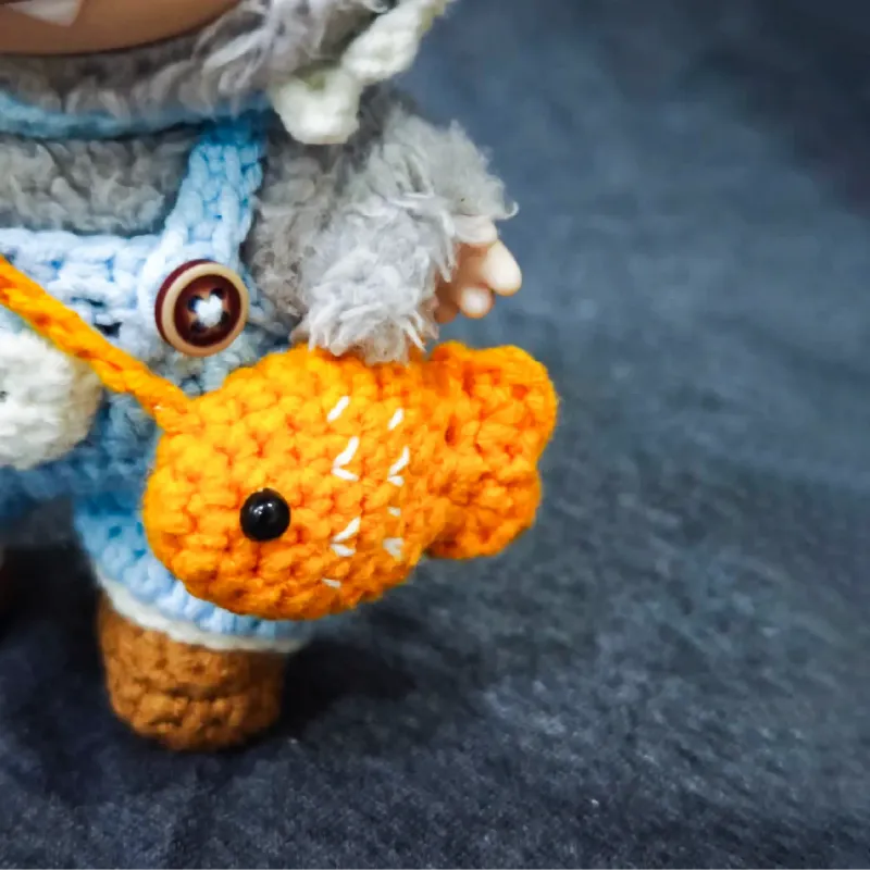 Funny fish crochet doll outfit pattern with bright orange fish accessory on handmade doll outfit