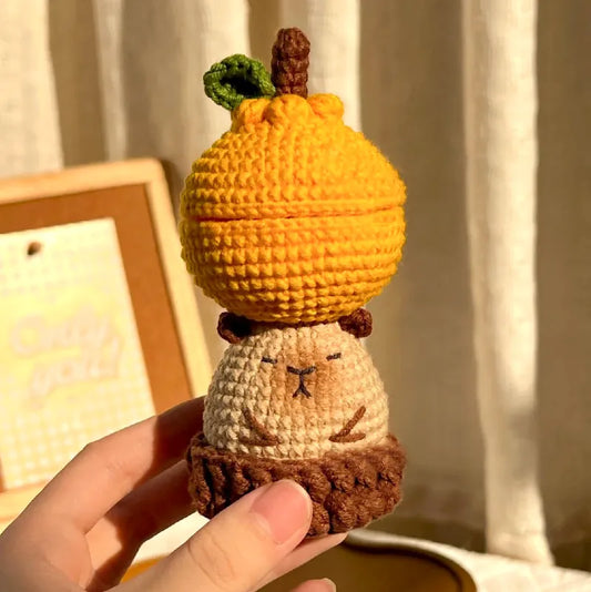 Hand holding a cute crochet capybara storage box pattern with orange pumpkin lid and brown base