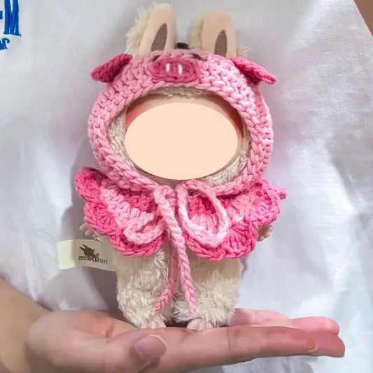 Hand holding a doll wearing a pink pig-themed crochet cape using doll cape crochet pattern free by The Knit Krazy