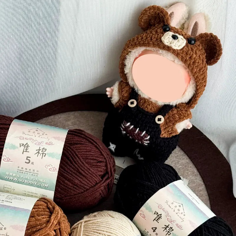 Handmade crochet doll wearing brown bear hat and black overalls surrounded by yarn balls