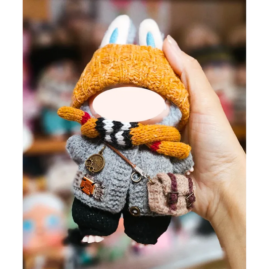 Hand holding a handmade knitted bunny doll wearing a mustard hat, gray coat, striped scarf, and carrying a small bag