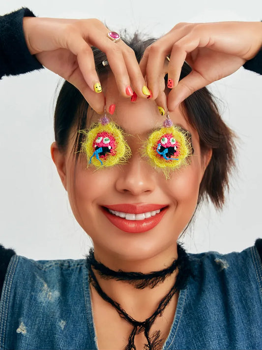 Handmade floral snake earrings held by smiling woman with colorful nails and denim jacket
