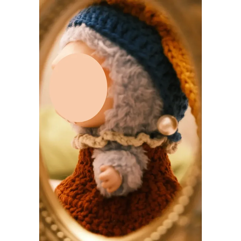 Close-up of a doll wearing girl with pearl earring doll clothes including knitted hat and dress with pearl detail