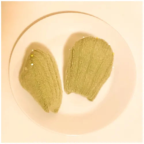 The Knit Krazy knitted madeleine dessert pattern showing two green shell-shaped knit pieces on a white plate