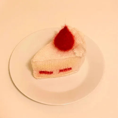 Knitted strawberry cake pattern slice with red strawberry on top displayed on white plate