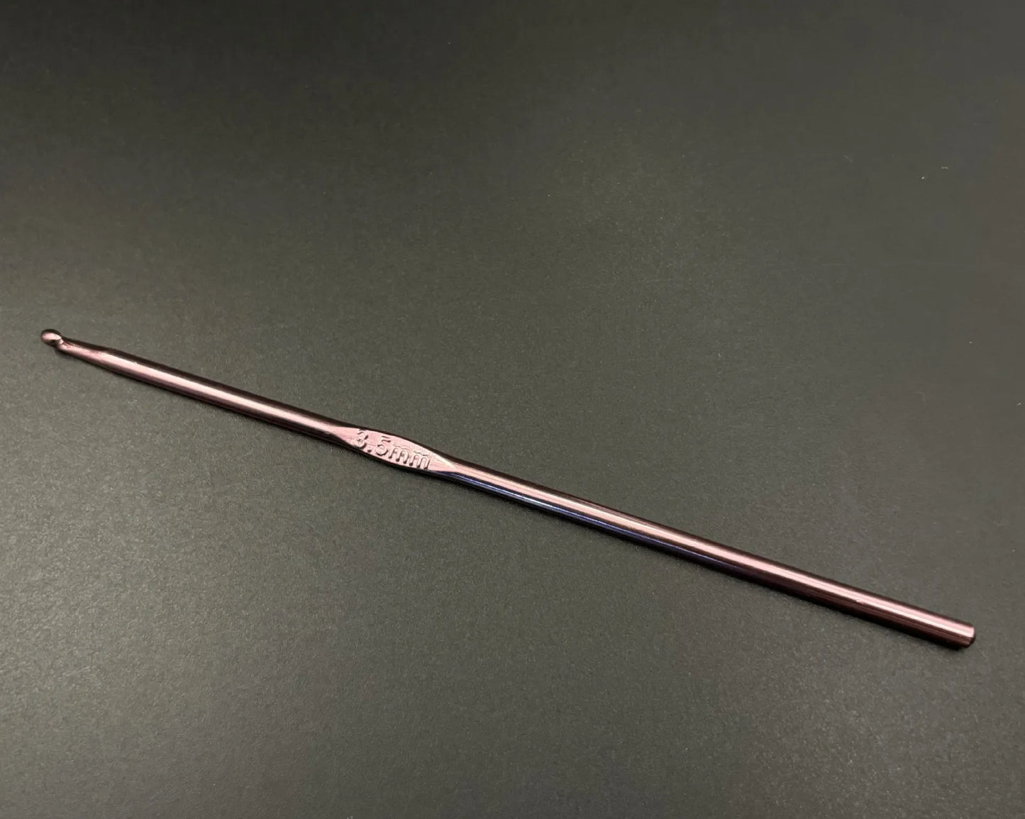Single rainbow aluminum crochet hooks set in rose gold color with ergonomic grip on dark background