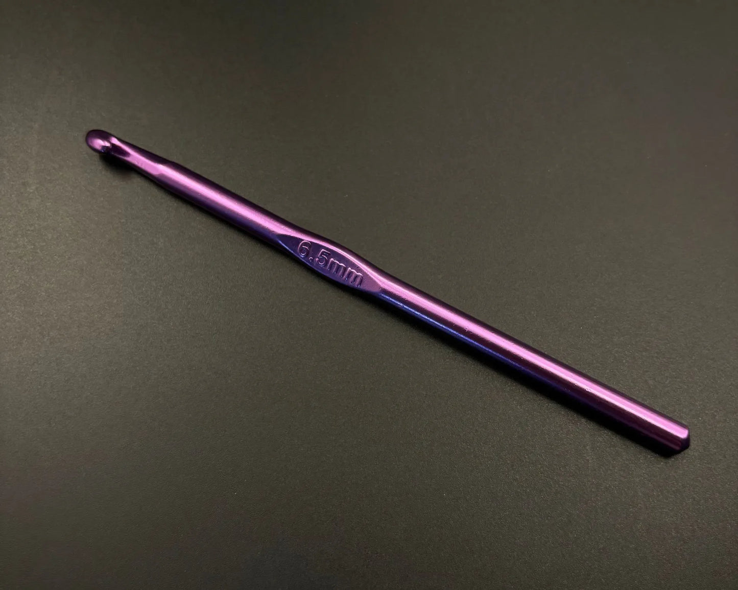 Single 6.5mm purple hook from rainbow aluminum crochet hooks set on black background
