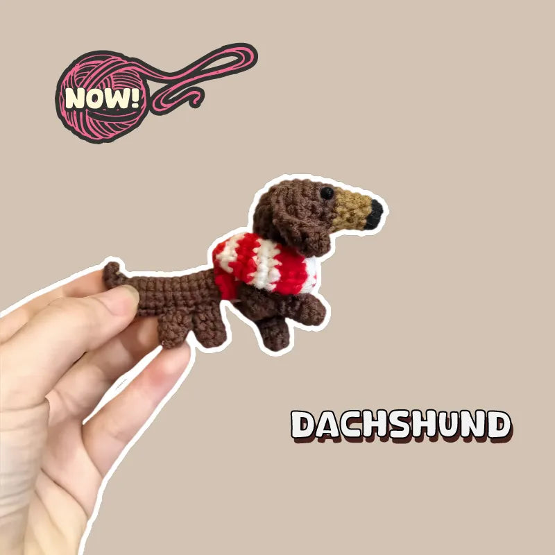Hand holding a brown crocheted dachshund amigurumi wearing a red and white sweater DIY dachshund amigurumi