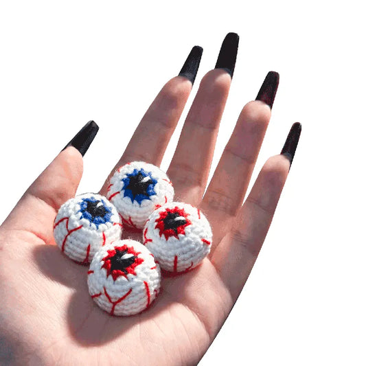 Hand holding four crochet eyeball toys with red and blue details on a white background