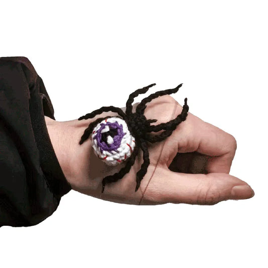 Hand wearing a spider-shaped ring with a purple center on a white background