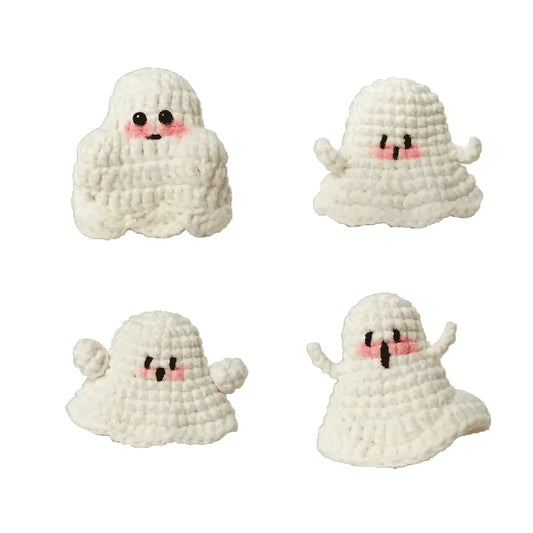 Four white crochet ghosts with black eyes and pink blush on a white background