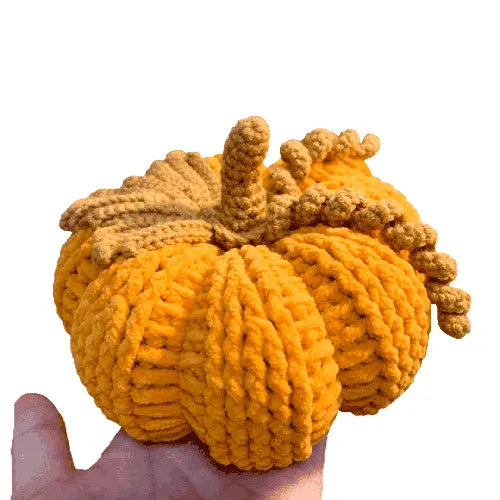 Knitted pumpkin toy held in a hand against a white background