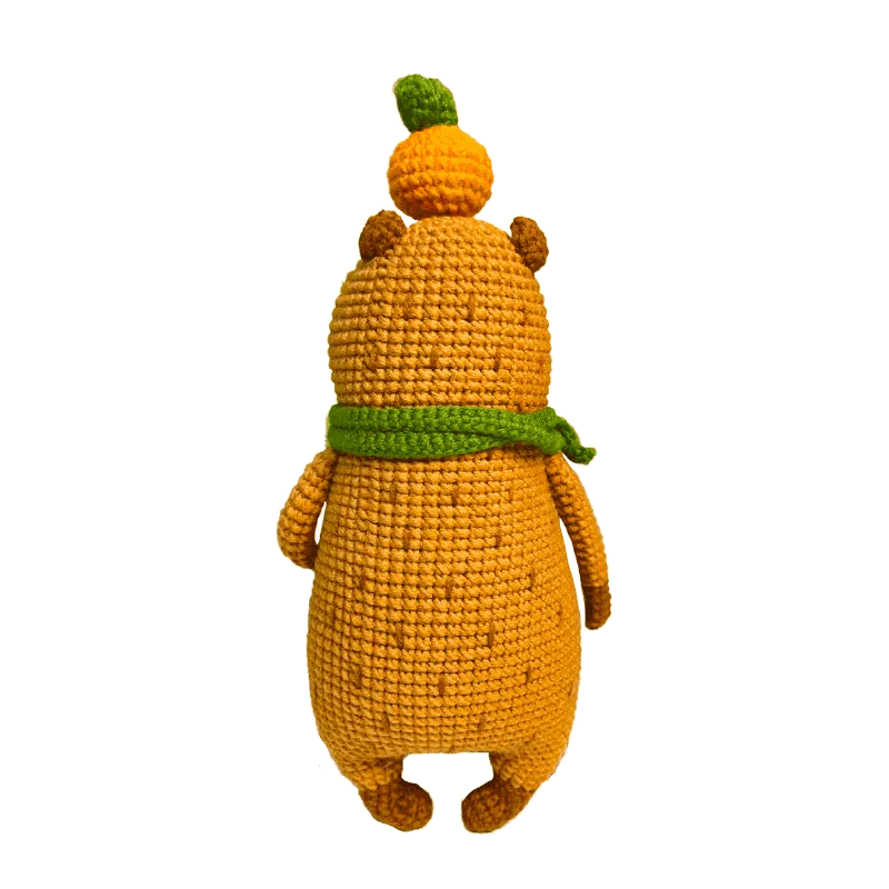 Handmade orange crochet toy shown from the back featuring the capybara amigurumi pattern with a green scarf and leaf detail
