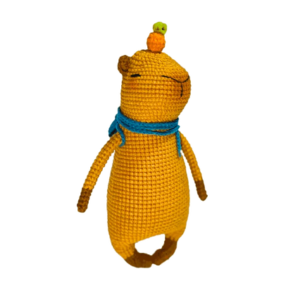 Handmade yellow capybara amigurumi pattern with blue scarf and small orange and green crocheted fruits on head