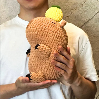 Person holding a handmade amigurumi capybara plushie with a yellow crocheted accessory amigurumi capybara plushie tutorial