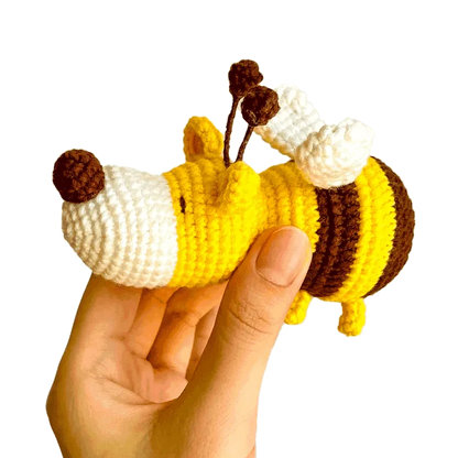 Hand holding a small yellow and brown crochet dog bee pattern with white wings and brown antennae