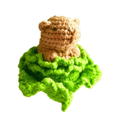Small brown crocheted capybara sitting on bright green crochet leaves using crochet capybara pattern