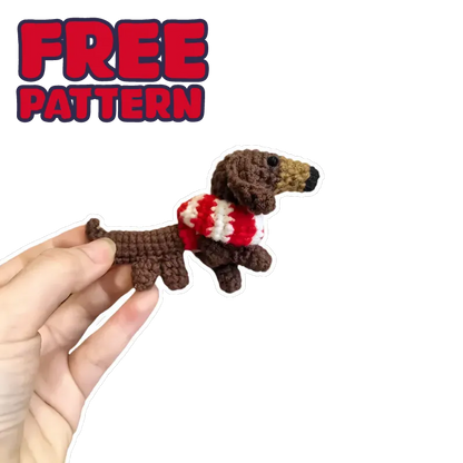 Hand holding a crochet DIY dachshund amigurumi with a red and white striped sweater on black background