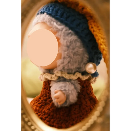 Close-up of a doll wearing girl with pearl earring doll clothes including knitted hat and dress with pearl detail