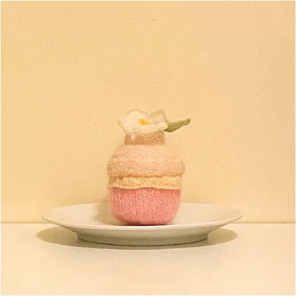 Handcrafted knitted cupcake pattern in pastel pink and cream colors displayed on a white plate