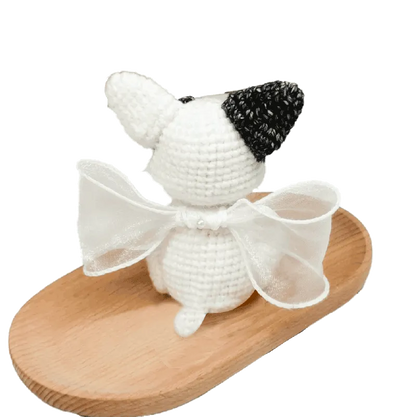 Handmade crochet French bulldog pattern plush figure with white and black yarn details and a white bow on wooden tray